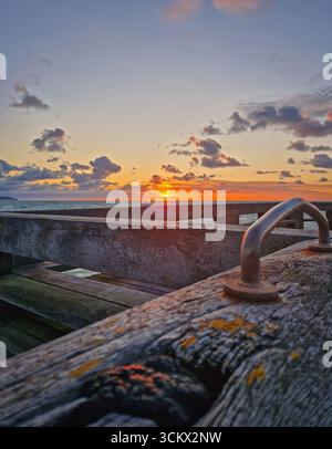 Atemberaubender Sonnenuntergang über dem Meer, während die Sonne unter dem Horizont eintaucht. Perspektive von einem hölzernen Pier, die strukturierten Dielen im Vordergrund zeigen. P Stockfoto