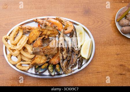 Nahaufnahme mit frittierten Meeresfrüchten, serviert auf einem Metallteller. Calamari-Ringe, Fische, Garnelen und Muscheln. Traditionelle mediterrane Küche, Gourmet-Foo Stockfoto