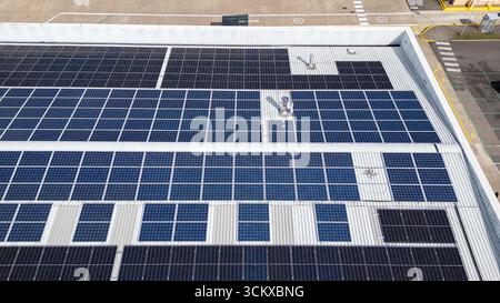Drohnenansicht von Solarpaneelen, die auf dem Dach eines Lagerhauses in einem Industriepark installiert sind und erneuerbare Energien und nachhaltige Stromerzeugung darstellen. Stockfoto