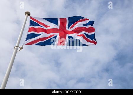 Die britische Union Jack-Flagge flattert im Wind vor einem klaren Himmel und symbolisiert Großbritannien, Erbe und nationale Identität. Stockfoto