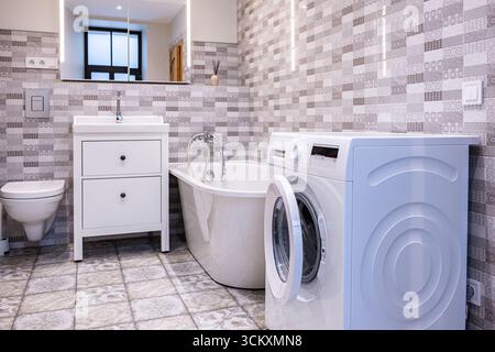 Stilvolles, modernes Bad mit funktionalem Waschbereich, Waschmaschine, eleganter Badewanne und geräumigem Design mit hellen Fliesen und modernem Design Stockfoto