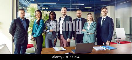 Eine Gruppe von Geschäftsleuten, die im Büro stehen und fröhlich auf die Kamera blicken und lächeln. Stockfoto