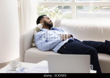 Müder erschöpfter junger Mann schläft nach der Computerarbeit auf der Couch Stockfoto