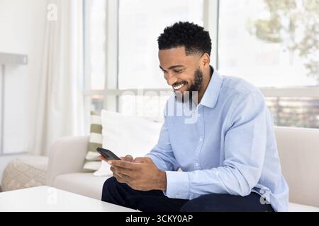 Glücklicher junger Hipster-Mann, der das Telefon auf dem Sofa benutzt und Spaß hat Stockfoto