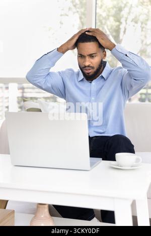 Verwirrter junger Freelancer schaut in Panik auf den Notebook-Bildschirm Stockfoto