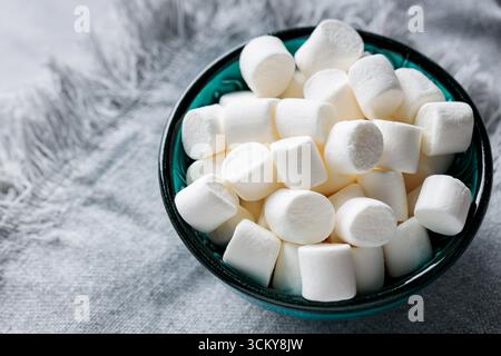 Marshmallows in türkisfarbener Schüssel auf Serviette aus grauem Leinen Stockfoto