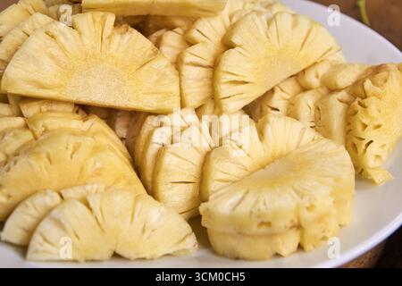Frisch geschnittene Ananasscheiben auf einer weißen Platte mit saftiger Textur und leuchtender gelber Farbe. Stockfoto