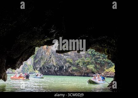 PHUKET, THAILAND - 12. NOVEMBER 2017: Touristen erkunden die malerische Höhle in Kajaks auf einem ruhigen grünen See, umgeben von felsigen Klippen und üppiger Vegetation. Stockfoto