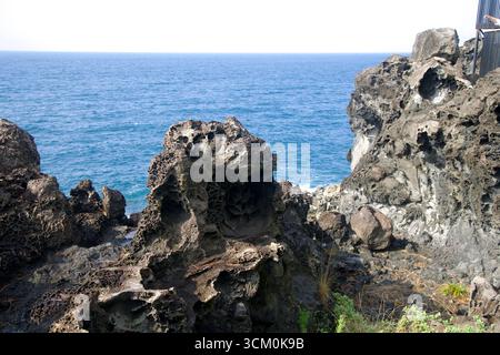 Vulkangesteine mit Wabenwaben und Löchern und Hohlräumen befinden sich am Klippenrand über dem blauen Ozean bei Daepo Jusangjeolli in Seogwipo. Stockfoto