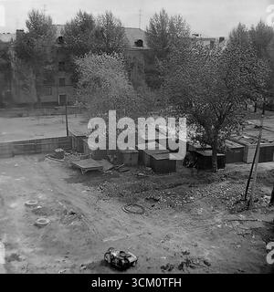 Die Hinterbühne eines großen Wiederaufbaus: Das Leben in den Höfen hinter dem zentralen Platz von Sloviansk, 1975-1976. Die Aufnahme fängt die chaotische Mischung des Wohnlebens ein, einschließlich selbstgebauter Schuppen und eines sowjetischen Motorrads mit Beiwagen, die während des großen Erneuerungsprojekts der Stadt fortgesetzt werden. Dieses Foto spiegelt den starken Kontrast zwischen dem zeremoniellen Stadtzentrum und dem authentischen, alltäglichen Leben seiner Bewohner wider und symbolisiert die friedliche, facettenreiche Welt der Donbass-Region, eine Welt, die lange vor den tragischen Ereignissen der Zukunft existierte Stockfoto