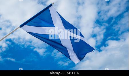 Die Nationalflagge Schottlands, das Saltyre oder St. Andrew’s Cross, fliegt auf einem Fahnenmast vor einem blauen Himmel mit verstreuten Wolken und symbolisiert Schottisch Stockfoto