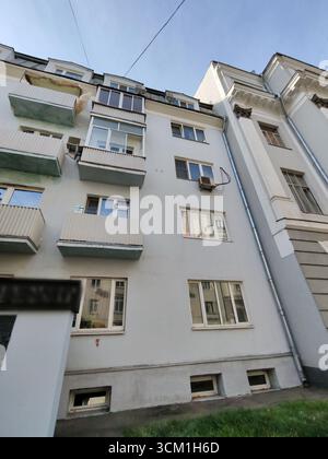 Ein graues Wohngebäude mit kleinen Balkonen, sichtbaren Klimaanlagen und Fenstern, die das umliegende Stadtbild reflektieren. Das Bild Stockfoto