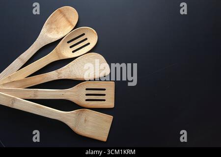 Küchenutensilien aus Holz mit Löffeln und Spateln auf schwarzem Hintergrund, natürliche Kochutensilien für zu Hause und im Restaurant. Stockfoto