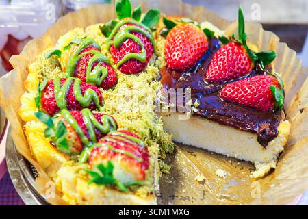 Halber Käsekuchen mit Matcha-Belag und glänzender Schokoladenglasur, dekoriert mit frischen Erdbeeren, cremigem Dessert perfekt für Gourmet-Bäckerei-Konzept. Stockfoto