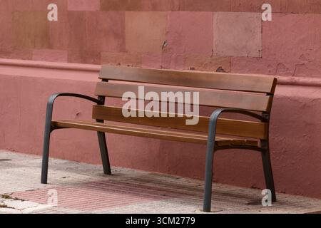 Bild einer Holzbank in einem öffentlichen Außenbereich neben einer braunen Wand, die auf einem gefliesten Boden sitzt Stockfoto