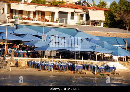 Eine große Taverne mit vielen blauen Sonnenschirmen und Liegen am Meer Stockfoto