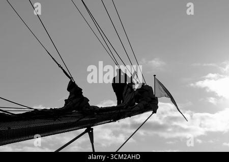 Crew-Silhouette, Arbeitslinien auf einem großen Schiffspriet auf der Sail 2025 in Amsterdam, Niederlande, hinterleuchteter Himmel mit Takelage und Rollsegeln deutlich abgebildet. Stockfoto