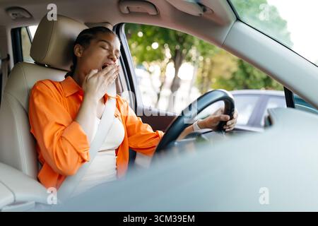 Müde afroamerikanische Frau gähnt beim Autofahren mit Sicherheitsgurt Stockfoto