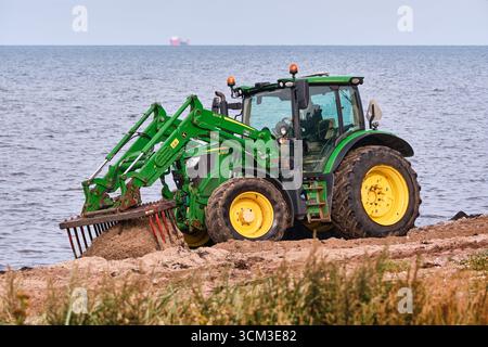 Helsingborg, Schweden; 12. August 2025: John Deere Traktor kratzt Algen aus Sand mit Rechen während der detaillierten Strandreinigung. Stockfoto