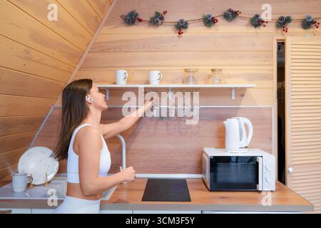 Frau organisiert Küchenregale in einer gemütlichen Holzhütte während der Tageslichtstunden. Stockfoto