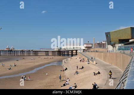 Strandszene mit Pier, modernem Gebäude und vielen Menschen an einem sonnigen Tag unter blauem Himmel. Stockfoto
