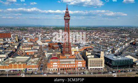 Ein Blick aus der Vogelperspektive auf eine Küstenstadt mit einem markanten hohen, roten Eisenturm, der das Stadtbild unter einem blauen Himmel mit weißen Wolken in Blackpool, Großbritannien, dominiert. Stockfoto