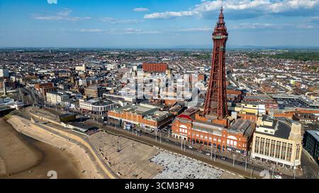 Aus der Vogelperspektive einer Küstenstadt mit einem markanten roten Turm, umgeben von Gebäuden und einem Strand unter blauem Himmel mit Wolken in Blackpool, Großbritannien. Stockfoto