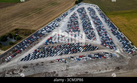 Aus der Vogelperspektive eines riesigen Autolagers mit Reihen geparkter Fahrzeuge, umgeben von landwirtschaftlichen Feldern und einem kleinen Teich am Copart Yard in York, U Stockfoto
