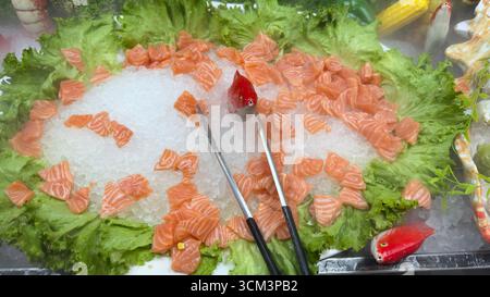Eine lebendige Präsentation von Lachsscheiben auf einem Bett aus Eis und Salat, die von zwei dekorativen Fisch- und Servierzangen akzentuiert wird. Stockfoto