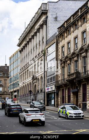 Eine Straßenszene mit Autos, einschließlich eines Polizeiautos, auf einer Straße, gesäumt von kunstvollen, mehrstöckigen Gebäuden in Newcastle upon Tyne, Großbritannien. Stockfoto