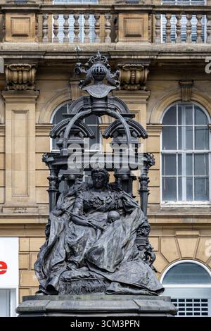 Eine detaillierte Bronzestatue der Königin Victoria, die auf einem Thron sitzt, ist zentral vor dem Hintergrund eines klassischen Steingebäudes mit Bogenwinde eingerahmt Stockfoto