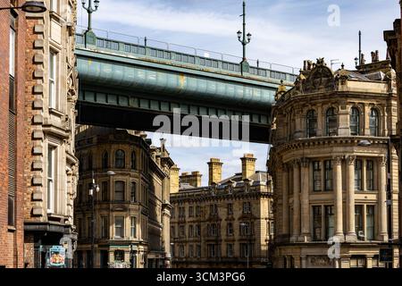 Eine urbane Szene mit einer großen, türkisfarbenen Brücke, die sich über kunstvoll verzierte Steinhäuser unter einem teilweise bewölkten Himmel in Newcastle upon Tyne, Großbritannien, erstreckt. Stockfoto