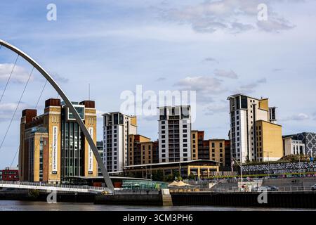 Ein modernes Stadtbild mit einer großen Bogenbrücke im Vordergrund, mit einem Fluss und verschiedenen Gebäuden im Hintergrund unter einem bewölkten Himmel in Newca Stockfoto