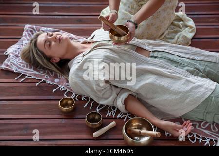 Frau, die sich einer Klangschüssel unterzieht und drinnen auf dem Boden liegt Stockfoto