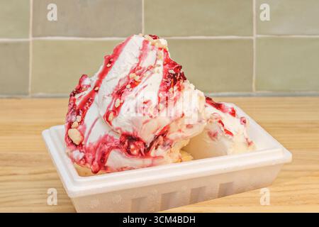 Käsekuchen-Eisbecher mit zerbröckelter Keksbasis, garniert mit Heidelbeerkompott und frischen Himbeeren, unwiderstehlich cremig Stockfoto