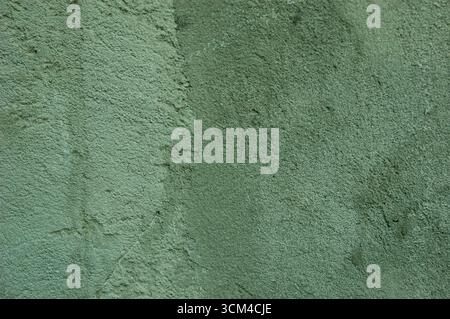 Eine graugrüne Betonwand mit Flecken und Kratzern, die einen strukturierten Hintergrund erzeugt. Stockfoto