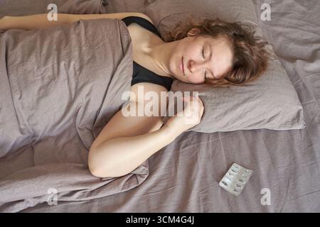 Junge kaukasische Frau schläft friedlich im Bett mit einer leeren Arzneimittelblase in der Nähe. Stockfoto