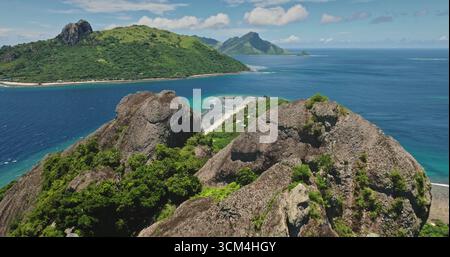 Fidschi, Insel Kuata: Grüne tropische Inseln erheben sich majestätisch aus türkisfarbenem Wasser eines ruhigen Ozeans und schaffen ein atemberaubendes Panorama natürlicher Schönheit. Niedriger Drohnenflug über Felsklippen Stockfoto