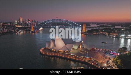 Das Opernhaus von Sydney mit der Sydney Harbour Bridge im Hintergrund beleuchtet Nachtlichter und bietet einen atemberaubenden Blick auf die Stadt mit farbenfrohen Himmel und beleuchteten Gebäuden. Drohne aus der Vogelperspektive Stockfoto