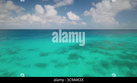 Atemberaubender Blick aus der Luft auf transparentes türkisfarbenes Wasser, das sanft mit dem tiefblauen Meer unter einem teilweise bewölkten Himmel verschmilzt und eine faszinierende Meereslandschaft schafft. Reisehintergrund, idyllisches exotisches Paradies Stockfoto