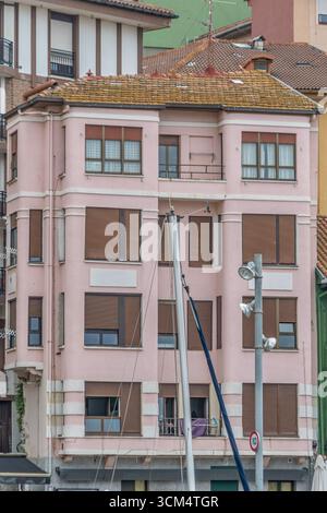 Pinkes Baskisches Wohngebäude mit braunen Fensterläden und moosbedecktem Dach in Nordspanien. Euskadi-Architektur, Mehrstöckiger Apartmentblock Stockfoto