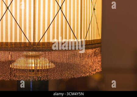 Eleganter Lampenschirm aus Vintage-Stoff mit Zierfransen und klassischem Streifendesign. Warm beleuchtet, verströmt er eine gemütliche, nostalgische Atmosphäre perfekt Stockfoto