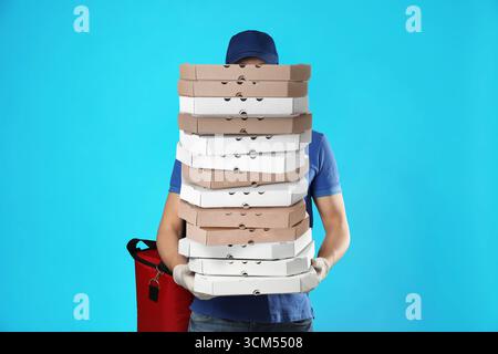 Der Zusteller hält viele Pizzaschachteln vor hellblauem Hintergrund Stockfoto