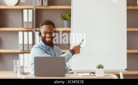 Freundlicher junger afroamerikanischer Mann Tutor zeigt Regeln des englischen an der Tafel und schaut auf den pc Stockfoto