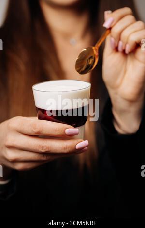 Frau mit cremigem Dessert mit Kirschgelee im Glas und goldenem Löffel Stockfoto