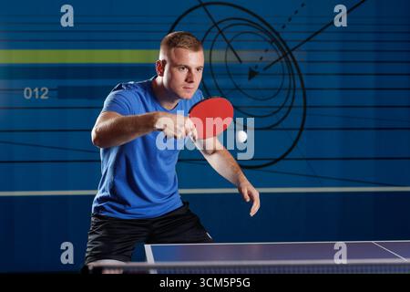 Junger Mann spielt Tischtennis und bereitet eine Vorhand mit rotem Paddel in einem Indoor Club vor. Dynamische Action mit sauberem Kopierraum für Sportangebote. Stockfoto