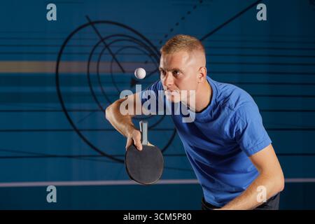 Ein junger Mann bereitet einen Tischtennistisch vor, der Ball schwimmt in einem Indoor Club. Dynamische Action- und Kopierflächen für Sportanzeigen und Coaching-Inhalte. Stockfoto