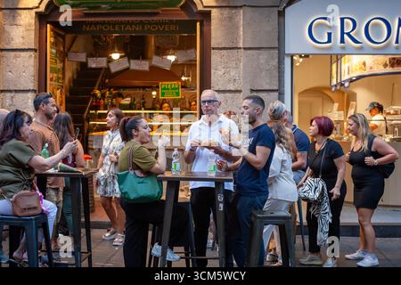Neapel, Italien - 11. September 2025: Tische im Freien in einer typischen neapolitanischen Pizzeria, bei denen einige Leute Street Food genießen und sich unterhalten. Stockfoto