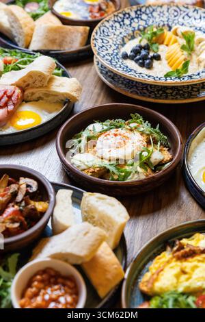 Köstliche Auswahl an Gourmet-Frühstücksgerichten, die auf Holztisch in einem gemütlichen Restaurant serviert werden Stockfoto