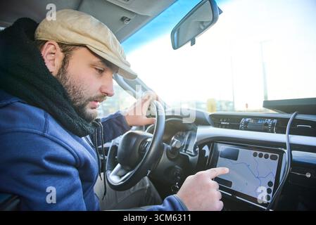 Ein Mann, der vor dem Anfahren seine Position und sein Ziel auf einer Karte auf dem Bildschirm seines Autos lokalisiert. Konzept: Einsatz von Technologie als Werkzeug Stockfoto